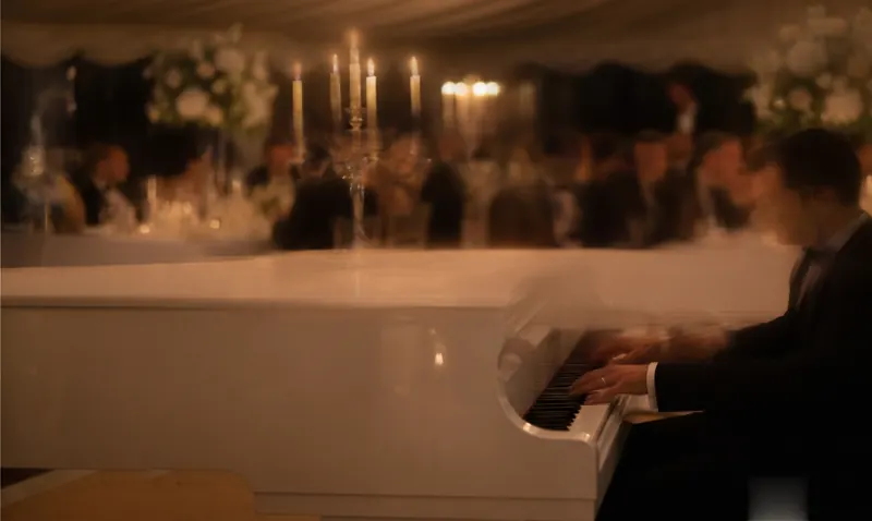 Pianist in black tie playing a white baby grand piano in a candlelit wedding marquee